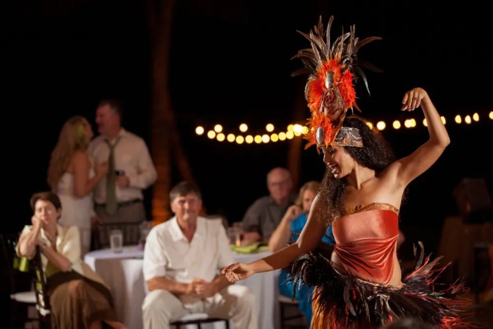 Woman in traditional dress dancing at an outdoor event, with seated guests watching.