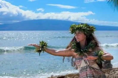Person in traditional attire dancing on a beach with ocean in background.