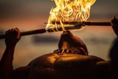 Person performing fire-eating with flames at sunset.