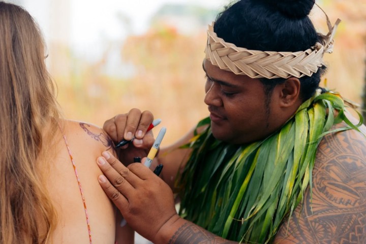 A person in traditional attire applying a temporary tattoo on a woman's shoulder.