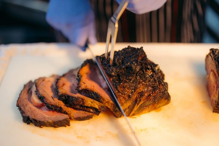 Person slicing smoked meat with gloved hands on a cutting board.