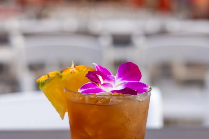 Cocktail with purple flower and pineapple on outdoor table.