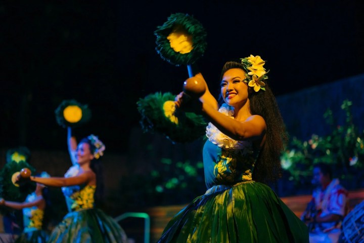 Women in traditional Hawaiian dresses performing a dance with yellow flowers.