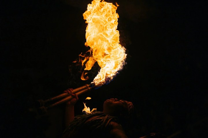 Performer breathing fire with two torches against a dark background.