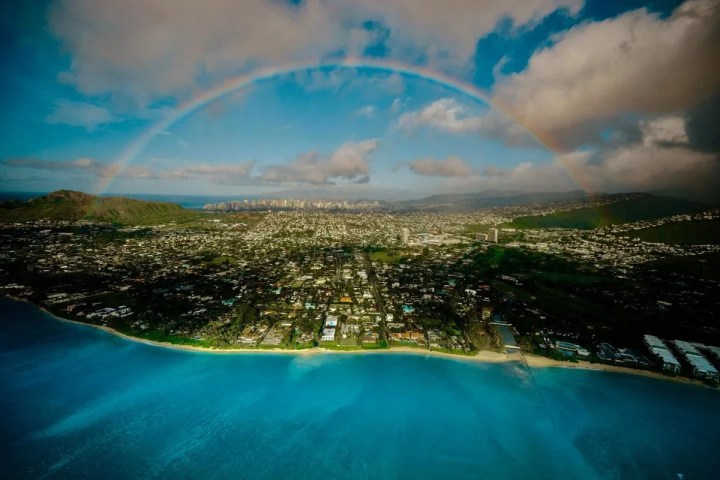 Aerial view of a city by the ocean, with a rainbow in the sky.